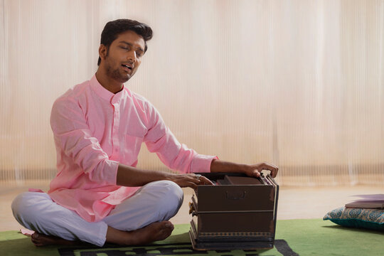 Portrait of young man playing harmonium at home