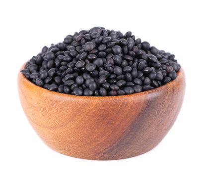 Black lentils in wooden bowl, isolated on white background. Dry beluga lentil grains pile.