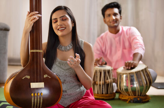 Close-up view of a young woman playing Tanpura and a man accompanying her on tabla