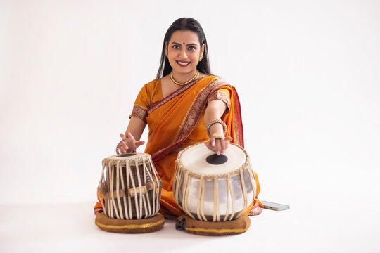 Portrait of cheerful woman in traditional outfit playing tabla