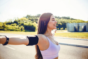 Happy fitness girl breathing fresh air on the road outstretching arms. Fitness woman stretching...