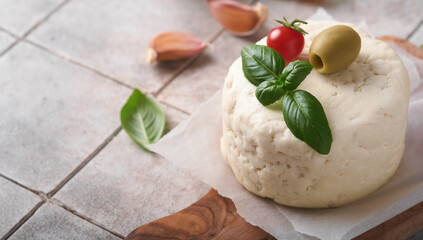 Ricotta cheese. Homemade Ricotta cheese with basil, garlic, tomatoes and green olives on parchment paperback and stand on old beige tiles background. Italian food.  Selective focus.