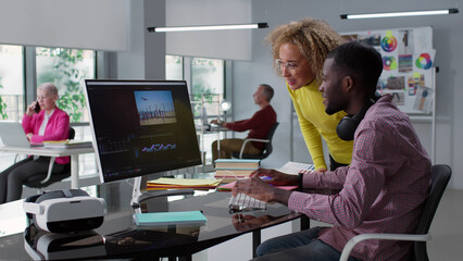 Diverse colleagues discuss video editing on computer screen working together in creative office