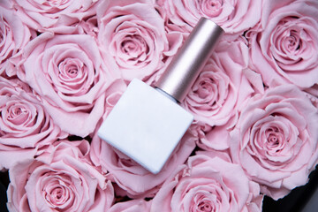Obraz na płótnie Canvas Nail polish bottle with white mockup for text lies on pink roses, background, 