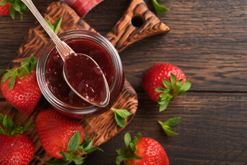 Strawberry jam. Strawberry jam in glass jar with fresh berries plate on an old wooden dark table background, closeup. Homemade strawberry fruity jam. Top view with copy space.
