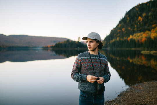 Young guy on lake shore in autumn forest at sunset