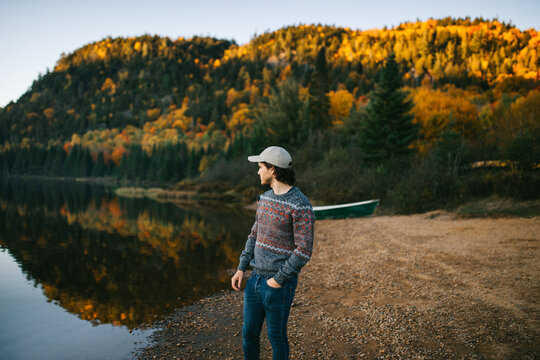 Stylish traveling guy standing at lakeside on autumn day