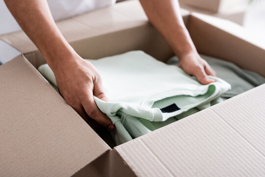 Cropped View Of African American Seller Putting Clothes In Carton Box In Online Web Store.