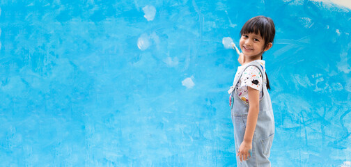 Banner of cute 5 years old asian little girl is smiling while painting the wall with water color at...