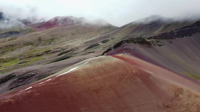 Man in red walking with Lama (Alpaka) on Rainbow Mountain Peak at Vinicunca Valley in Peru. Aerial footage. Red Valley.