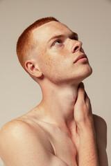 Close-up portrait of handsome young red-haired man posing isolated over grey studio background....