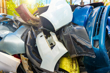 Close-up of plastic fiber car bumpers in a car junkyard, taken in backlit and sun glare. Plastic raw materials, collection of plastic waste for recycling.