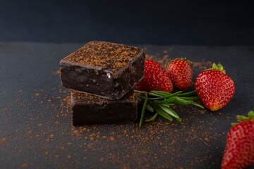 Sweet candies sprinkled with cocoa and next to strawberries. Delicious dessert. Bird's milk in chocolate with cocoa and strawberries. Chocolate covered strawberries