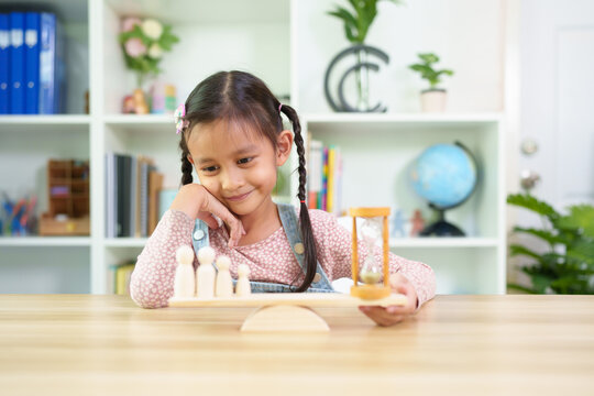 Cute asian little girl's hands trying to balance the family member model and hourglass on wooden scale, concept of balance of quality time and family life, work-life balance and parent time for kid.