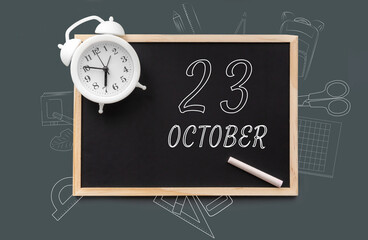 october 23. 23th day of month, calendar date. Blackboard with piece of chalk and white alarm clock on green background. Concept of day of year, time planner, autumn month