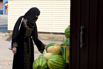 A Muslim woman in national clothes inspects watermelons and melons city market.
