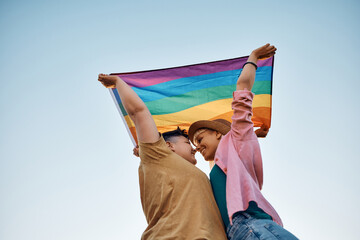 Young female couple in love with rainbow flag against the sky.