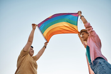 Below view of happy lesbian couple holding rainbow flag against the sky.