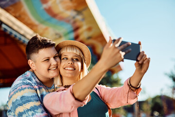 Naklejka premium Happy female couple taking selfie with cell phone at amusement park.