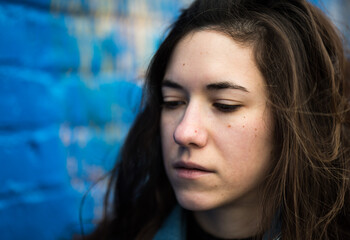 Close up of an attractive 27 year old woman with brown hair, against a blue wall