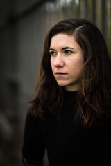 Fototapeta premium Portrait of a 27 year old white woman, dressed in black, standing against a metal fence