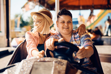 Young lesbian and her girlfriend driving bumper car at amusement park.