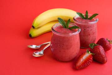 Smoothie with strawberry and banana in the glass jars on the red background. Copy space. Close-up.