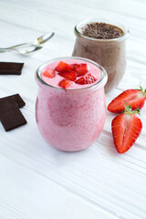 Natural milk yogurt with strawberry and chocolate in the glass jar on the white wooden background. Location vertical.