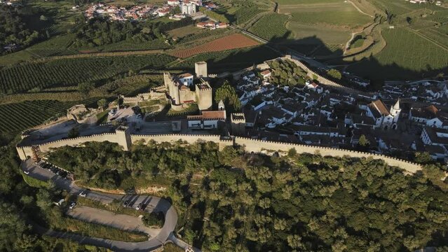 Ancient castle fortress in Portugal drone flyby with green fields on sunny day. Old European middle ages town Obidos with modern bridge highway in the background.