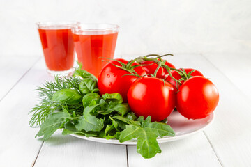Fresh tomatoes and greens on a white plate on a light wooden background. Copy space