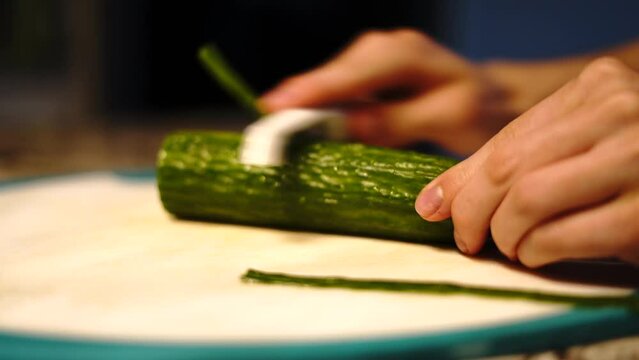 Person slowly peeling nutritious cucumber with vegetable scraper, home kitchen