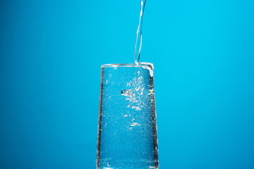 Water is poured into a glass on a blue background. Pure drinking water.