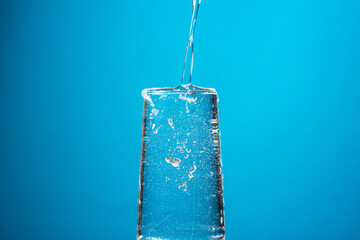 Water is poured into a glass on a blue background. Pure drinking water.