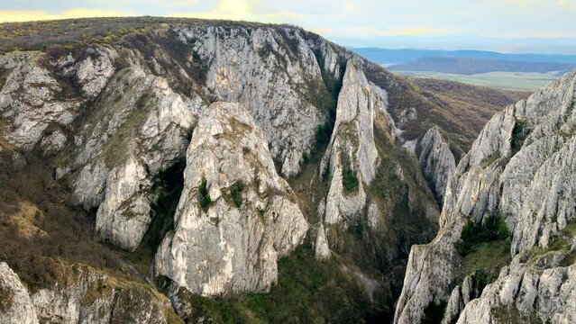 Aerial drone view of a rocky canyon in Romania. Rocky cliffs with sparce vegetation. Fields in the distance