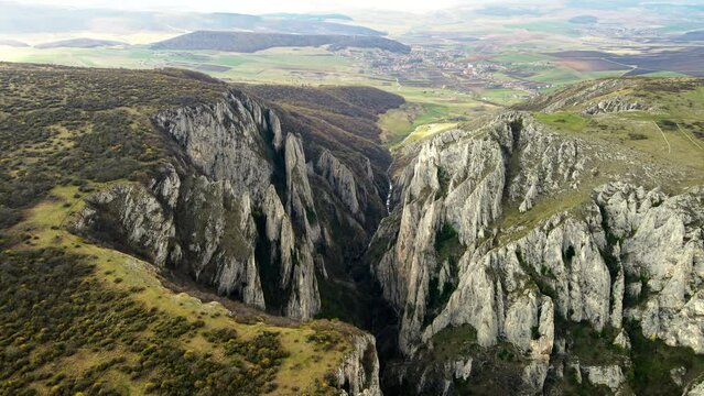 Aerial drone view of a rocky canyon in Romania. Rocky cliffs with sparce vegetation. Fields and hills around
