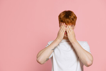 Portrait of young red-headed man in white t-shirt posing isolated over pink studio background. Concept of youth, fashion, emotions, facial expression