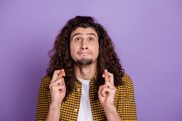 Photo of young man look empty space crossed fingers pray wish luck isolated over purple color background