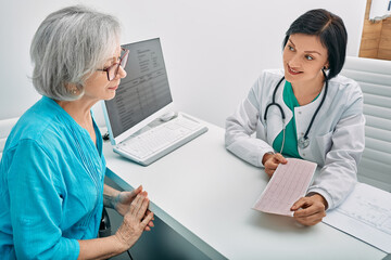 Positive doctor consulting senior woman on results of cardiogram and test. Diagnostic heart...