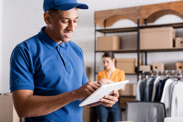 Smiling african american deliveryman using digital tablet in online web store.