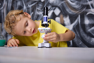 Boy lifted glasses on head and carefully studied structure of microscope starting from its base to...
