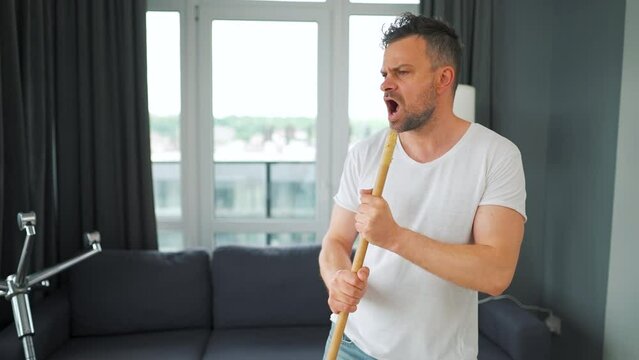 Man cleaning the house and having fun dancing and singing with a broom. Slow motion