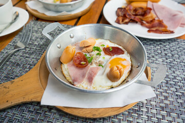 The breakfast menu pan-fried egg with toppings served with a hot pan on the dining table consisting of sausage, Chinese sausage, ham, minced pork and shredded scallions.