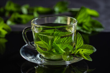 Hot cup of tea with fresh mint leaf on black background