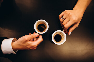 A man and a woman are holding cups of coffee in their hands. A woman has a ring on her finger