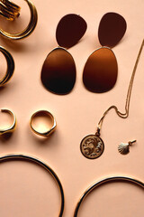 Various gold jewelry and pearl hair clips on peach colored background. Flat lay.