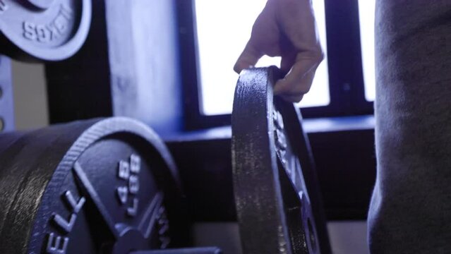 Weightlifter adding heavy 45lb steel plate to powerlifting bar for strength training
