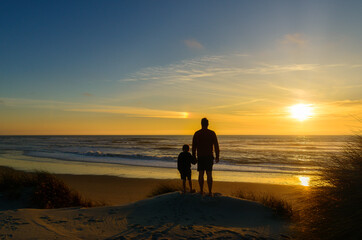 Boy holding the hand of his father while looking the sunset at the sea