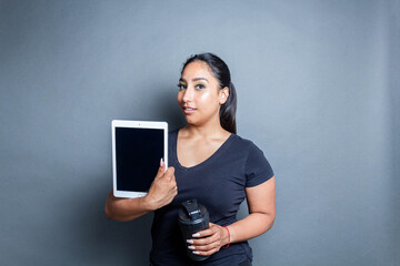 sporty hispanic young woman holding shaker and showing tablet screen