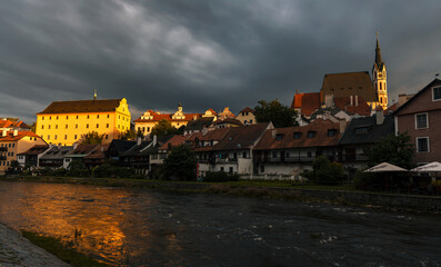 St. Vitus Church and picturesque old town houses on the banks of Vltava river in Cesky Krumlov, Czech Republic. Beautiful sunset light, stormy clouds, reflections in the river.