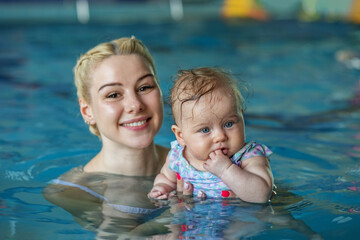 Young beautiful blonde mother with baby in pool. Concept of sport, training and family